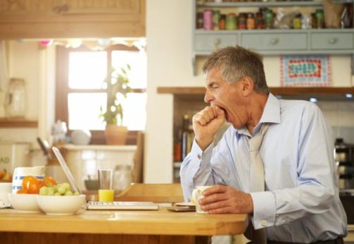 Man yawning at kitchen table with laptop.